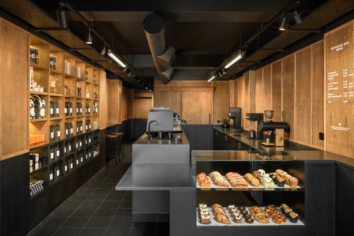 Modern coffee shop interior with wooden walls, shelves, and a counter displaying pastries.