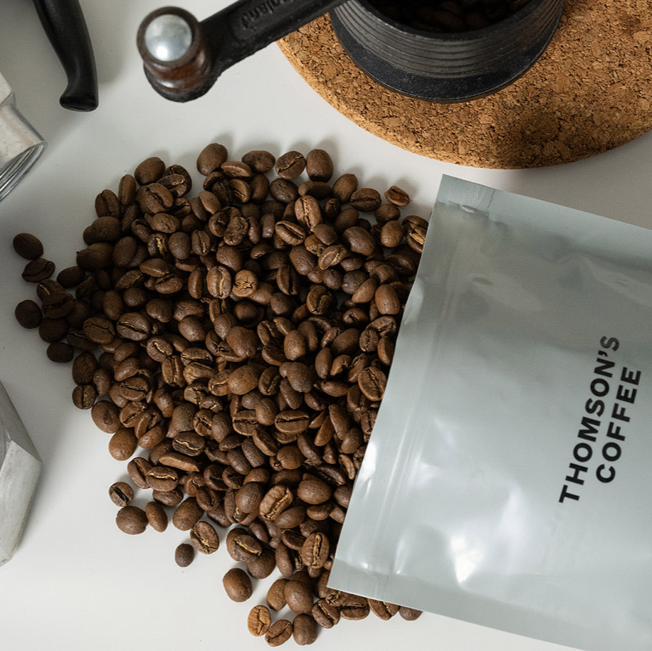 Coffee beans and a package of Thomson's Coffee on a white surface.